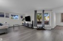 Spacious living area featuring wood-finish flooring, white walls, and bright windows - #113 2508 50 St Nw, Edmonton, AB 