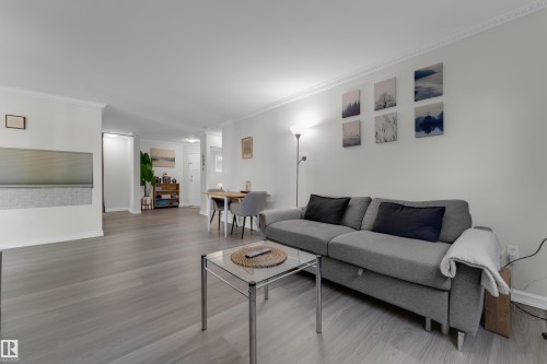 Spacious living area featuring wood-finish flooring, white crown molding, and neutral wall tones - #113 2508 50 St Nw, Edmonton, AB 