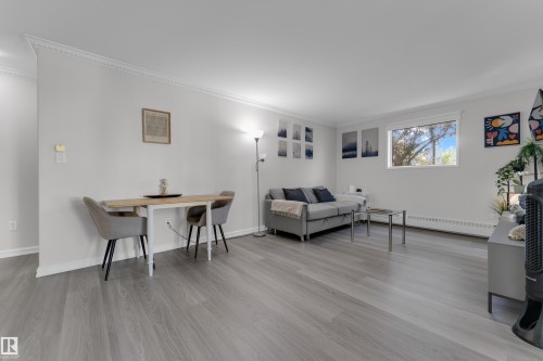 Light wood-finish flooring, white walls, crown molding, and a visible window - #113 2508 50 St Nw, Edmonton, AB 