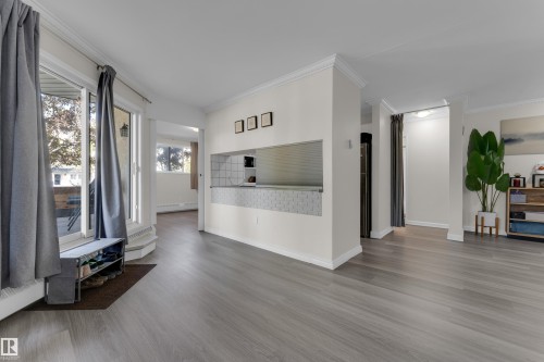 Wood-finish flooring, white crown molding, white baseboards, and a pass-through window with tile detail - #113 2508 50 St Nw, Edmonton, AB 