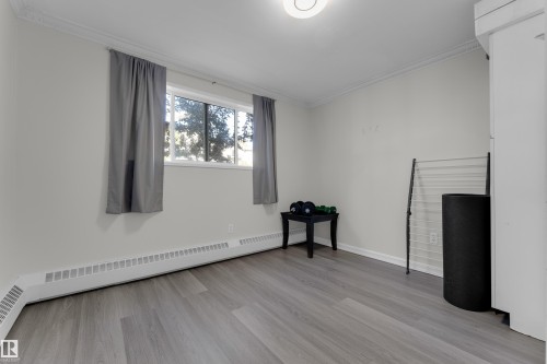 Light-toned wood-finish flooring, white walls, crown molding, a window, and a ceiling-mounted light fixture - #113 2508 50 St Nw, Edmonton, AB 