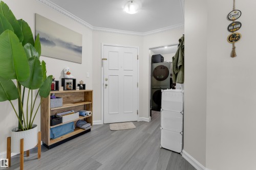 Entryway featuring wood-finish flooring, crown molding, a built-in laundry closet with stacked appliances, and a single paneled entry door - #113 2508 50 St Nw, Edmonton, AB 