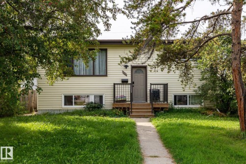 Split-level residence featuring light-colored siding, a dark-toned front door, and a wooden deck with black metal railings - 10972 157 Street Nw, Edmonton, AB 