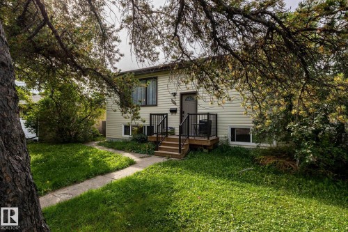 Exterior featuring light-colored siding, a front entry with a storm door, an elevated wood-finish deck with black railings, and a concrete pathway - 10972 157 Street Nw, Edmonton, AB 