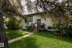 Exterior featuring light-colored siding, a front entry with a storm door, an elevated wood-finish deck with black railings, and a concrete pathway - 
