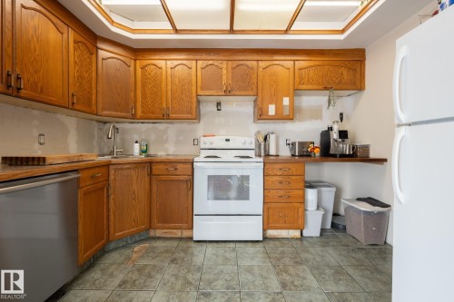 Kitchen featuring wood cabinetry, stainless steel dishwasher, white range, and tiled flooring - 10972 157 Street Nw, Edmonton, AB 