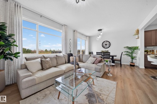 Open-concept living area featuring large windows, wood-finish flooring, and a dining space with a contemporary pendant light fixture - 4104 3 Avenue Sw, Edmonton, AB 