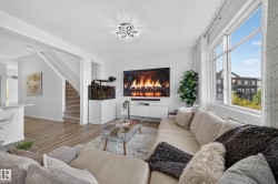Bright living area featuring large windows, wood-finish flooring, a built-in entertainment console, a contemporary ceiling light fixture, and a carpeted staircase - 