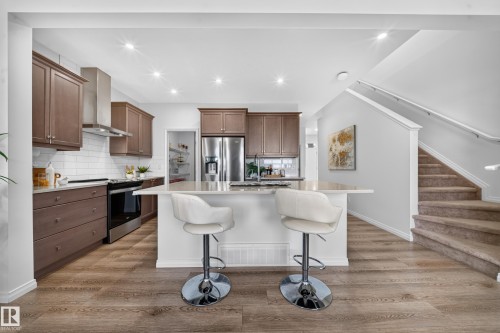 Kitchen featuring wood-finish flooring, recessed lighting, white subway tile backsplash, stainless steel appliances, and a central island with a light-toned countertop - 4104 3 Avenue Sw, Edmonton, AB 
