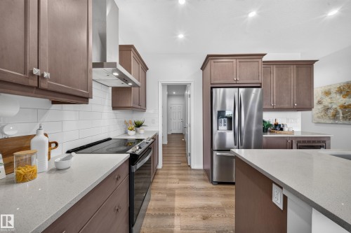 Recessed lighting illuminates the kitchen featuring wood-finish cabinetry, stainless steel appliances, a white subway tile backsplash, light-toned countertops, and wood-finish flooring - 4104 3 Avenue Sw, Edmonton, AB 
