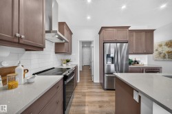 Recessed lighting illuminates the kitchen featuring wood-finish cabinetry, stainless steel appliances, a white subway tile backsplash, light-toned countertops, and wood-finish flooring - 