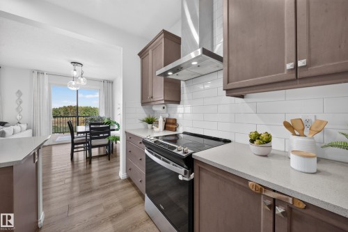 Kitchen featuring wood-finish cabinetry, light-toned countertops, a stainless steel range hood, and a white subway tile backsplash - 4104 3 Avenue Sw, Edmonton, AB 