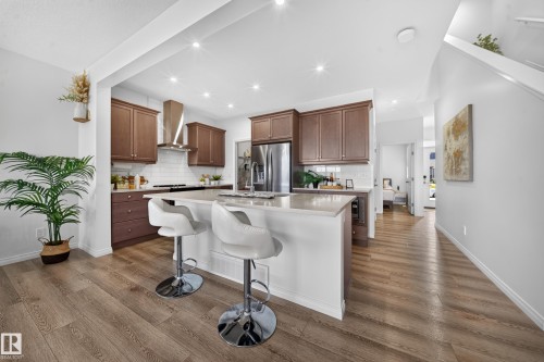 Kitchen featuring wood-finish flooring, full-height cabinetry, stainless steel appliances, a subway tile backsplash, and a central island with a light-toned countertop - 4104 3 Avenue Sw, Edmonton, AB 