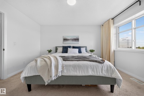 Bright bedroom featuring carpet flooring, crisp white walls, a large window, and a flush mount ceiling light - 4104 3 Avenue Sw, Edmonton, AB 