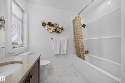 White subway tile shower surround, white bathtub, vanity with integrated sink, light-colored countertop, and white tile flooring with veining - 4104 3 Avenue Sw, Edmonton, AB 