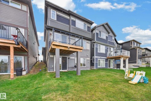 Expansive backyard with a manicured lawn, multi-level dwelling, and an upper-level balcony with metal railings - 4104 3 Avenue Sw, Edmonton, AB 