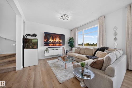 Expansive living area featuring light wood-finish flooring, a large window, and a white floating media console - 4104 3 Avenue Sw, Edmonton, AB 