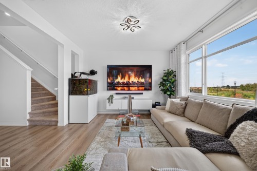 Bright living area featuring large windows, wood-finish flooring, a built-in media console, and a contemporary ceiling fixture - 4104 3 Avenue Sw, Edmonton, AB 