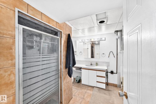 Glass-enclosed shower with frosted detailing, tiled shower surround, vanity with integrated sink, white cabinetry, and a full-length mirror - 44 Habitat Crescent Nw, Edmonton, AB 