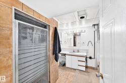 Glass-enclosed shower with frosted detailing, tiled shower surround, vanity with integrated sink, white cabinetry, and a full-length mirror - 