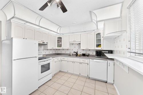 Kitchen featuring white cabinetry, tile flooring, and integrated white appliances - 44 Habitat Crescent Nw, Edmonton, AB 