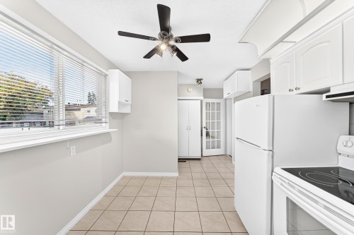 Bright kitchen area featuring a large window, tiled flooring, white cabinetry, a ceiling fan, and a glass-paneled door - 44 Habitat Crescent Nw, Edmonton, AB 
