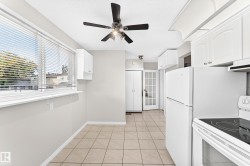 Bright kitchen area featuring a large window, tiled flooring, white cabinetry, a ceiling fan, and a glass-paneled door - 