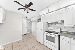 White kitchen cabinetry with complementary white appliances, tile flooring, and a ceiling fan with integrated lighting - 