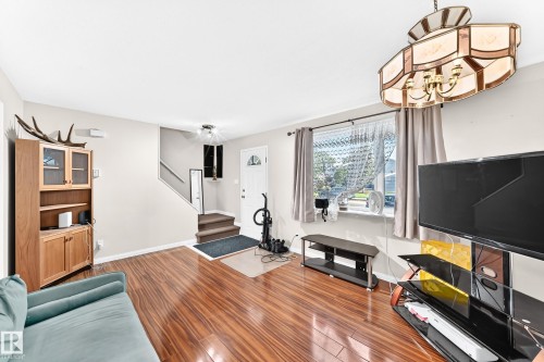 Wood-finish flooring throughout, a decorative chandelier, and a white entry door with a frosted glass insert - 44 Habitat Crescent Nw, Edmonton, AB 