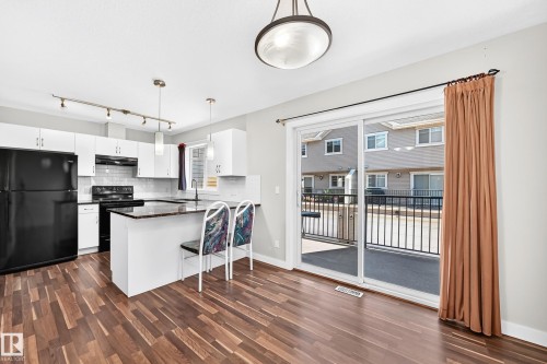 Kitchen featuring wood-finish flooring, white cabinetry, black appliances, a central island with a dark countertop, and a sliding glass door leading to a patio - #39 7289 South Terwillegar Nw, Edmonton, AB 