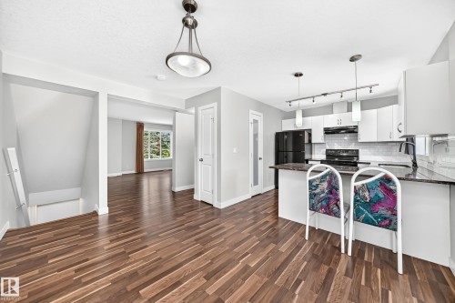 Wood-finish flooring throughout, kitchen with white cabinetry, dark countertops, and stainless steel appliances, and a built-in kitchen island - #39 7289 South Terwillegar Nw, Edmonton, AB 