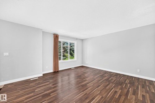 Spacious room featuring wood-finish flooring, light gray walls, white trim, and a multi-pane window - #39 7289 South Terwillegar Nw, Edmonton, AB 