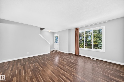Expansive living area featuring rich wood-finish flooring, a large multi-pane window, and a white entry door with decorative glass - #39 7289 South Terwillegar Nw, Edmonton, AB 