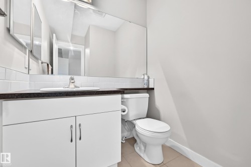 White vanity with dual cabinet doors, integrated sink, dark countertop, and a large wall-mounted mirror - #39 7289 South Terwillegar Nw, Edmonton, AB 