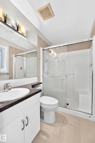 Vanity with an integrated sink and dark countertop, glass-enclosed shower, tiled flooring, and modern overhead lighting - #39 7289 South Terwillegar Nw, Edmonton, AB 