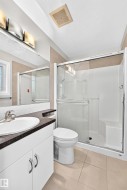 Vanity with an integrated sink and dark countertop, glass-enclosed shower, tiled flooring, and modern overhead lighting - 