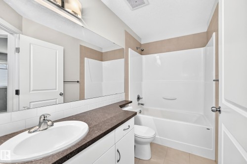 Bathroom featuring a white subway tile backsplash, dark countertop, white vanity cabinetry, integrated sink, and a combination tub and shower unit - #39 7289 South Terwillegar Nw, Edmonton, AB 