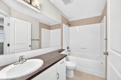 Bathroom featuring a white subway tile backsplash, dark countertop, white vanity cabinetry, integrated sink, and a combination tub and shower unit - 