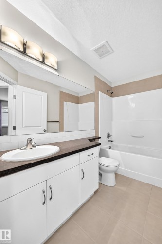 Bathroom featuring a single vanity with white cabinetry, a dark countertop, an undermount sink, and a large mirror - #39 7289 South Terwillegar Nw, Edmonton, AB 