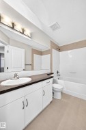 Bathroom featuring a single vanity with white cabinetry, a dark countertop, an undermount sink, and a large mirror - 