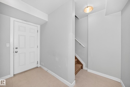 Entryway featuring a paneled door, tile flooring, and wood-finish stairs with a handrail - #39 7289 South Terwillegar Nw, Edmonton, AB 