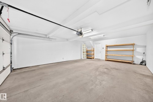 Spacious garage featuring a concrete floor, built-in shelving, and white overhead door - #39 7289 South Terwillegar Nw, Edmonton, AB 