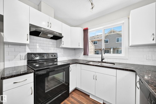 Kitchen featuring white cabinetry, dark countertops, white subway tile backsplash, and wood-finish flooring - #39 7289 South Terwillegar Nw, Edmonton, AB 