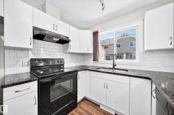 Kitchen featuring white cabinetry, dark countertops, white subway tile backsplash, and wood-finish flooring - 