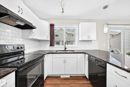 U-shaped kitchen featuring white cabinetry, dark countertops, a black range with an overhead exhaust, and a white subway tile backsplash - #39 7289 South Terwillegar Nw, Edmonton, AB 