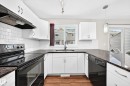 U-shaped kitchen featuring white cabinetry, dark countertops, a black range with an overhead exhaust, and a white subway tile backsplash - #39 7289 South Terwillegar Nw, Edmonton, AB 