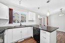 Kitchen featuring white cabinetry, dark stone countertops, a black sink faucet, stainless steel appliances, and wood-finish flooring - #39 7289 South Terwillegar Nw, Edmonton, AB 