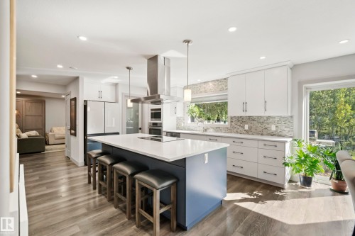 Kitchen featuring a large island with seating, pendant lighting, stainless steel range hood, built-in appliances, and wood-finish flooring - 49279 Rge Rd 240, Rural Leduc County, AB 