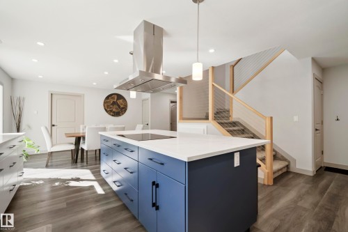 Open-concept living area with wood-finish flooring, a contemporary kitchen island with a cooktop, a stainless steel range hood, and a light wood and cable railing staircase - 49279 Rge Rd 240, Rural Leduc County, AB 