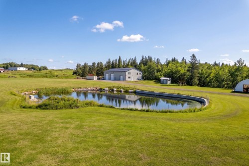 Expansive green space featuring a pond with a concrete retaining wall, a detached multi-bay structure, and a secondary outbuilding - 49279 Rge Rd 240, Rural Leduc County, AB 